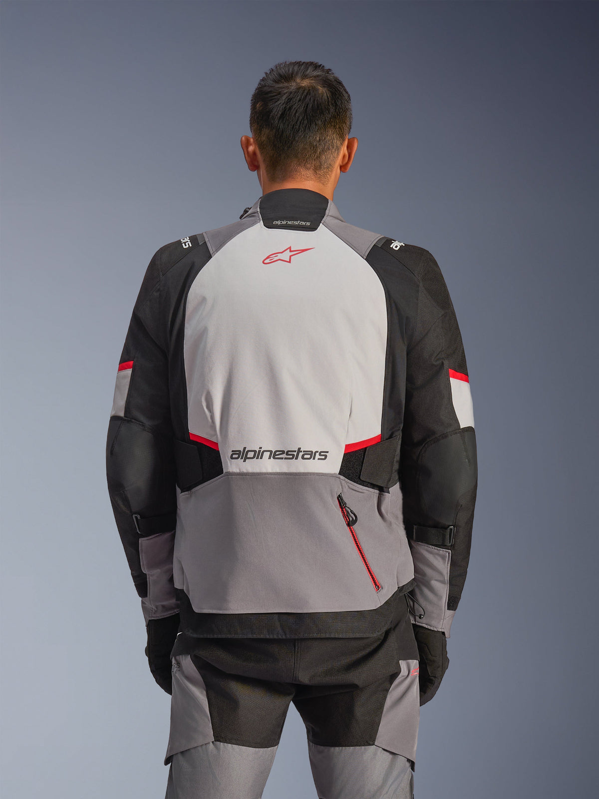 Kurtka Alpinestars Andes V4 Drystar®, widok z tyłu, ciemnoszara, jasnoszara, czarna i jaskrawoczerwona, czerwone logo Astar i napis Alpinestars na plecach, wzmocnione panele i czerwona kieszeń na zamek, odzież motocyklowa typu adventure