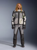Męski model z długimi blond włosami ubrany w kurtkę Andes V4 Drystar® w kolorach ciemnoszarym, jasnoszarym, czarnym i żółtym fluo, z dopasowanymi spodniami motocyklowymi adventure i czarnymi butami, kompletny techniczny strój motocyklowy do turystyki w każdych warunkach pogodowych.