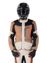 Alpinestars ST-1 Waterproof Jacket, Dark Khaki Sand Black Red Fluo, worn by a rider with a black helmet and gloves, adventure touring gear with beige and brown panels and bright red fluo accents, front view on a white background.