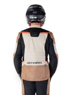 Alpinestars ST-1 Waterproof Jacket, Dark Khaki Sand Black Red Fluo, Rear view, adventure touring motorcycle jacket featuring a large sand-colored back panel, black sleeves, and red fluorescent accents, shown on a rider with a black helmet.