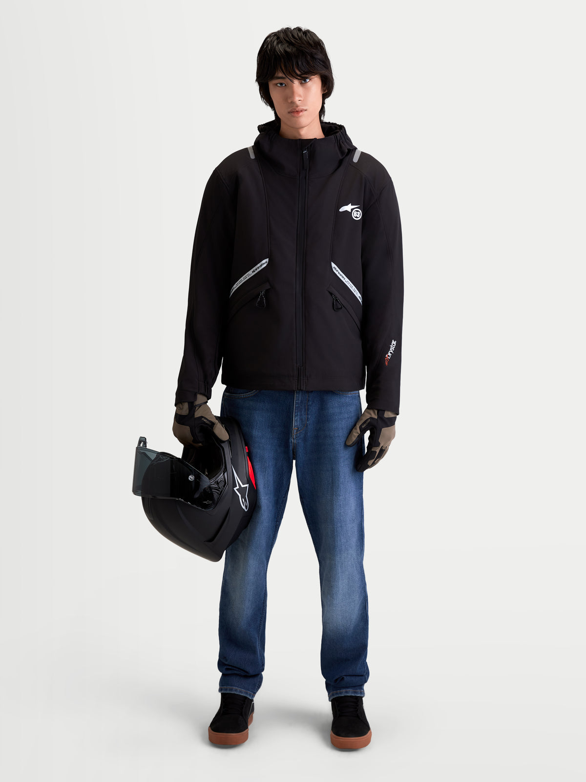 Alpinestars C 5 Drystar kurtka motocyklowa męska miejska współczesna, czarna, widok z przodu na modelu w jeansach i rękawicach trzymającym kask, prezentująca wodoodporną konstrukcję softshell i zintegrowany kaptur