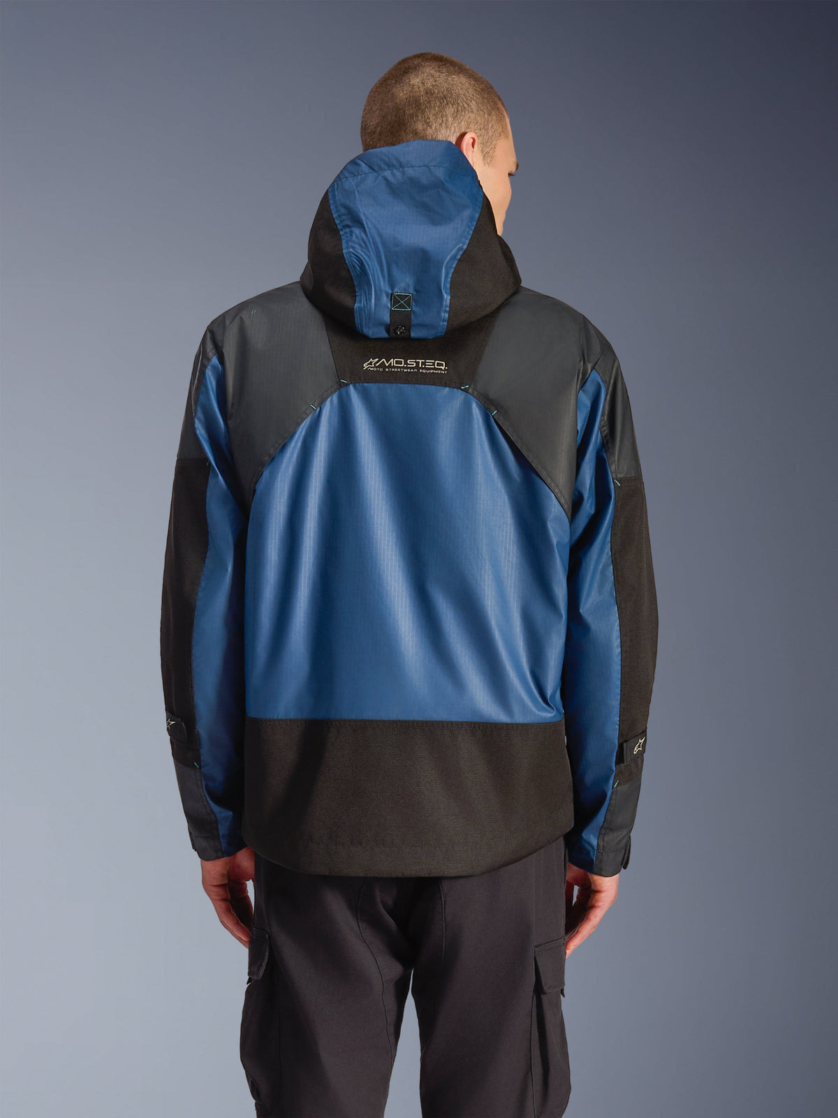 Alpinestars Mospher Waterproof Jacket w kolorze Black Dark Petrol, widok z tyłu motocyklowej parki z niebieskimi panelami ripstop i czarnymi wzmocnionymi sekcjami, logo MO.ST.EQ. w górnej części pleców, nowoczesny miejski design taktyczny