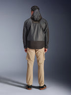 Alpinestars Mospher Waterproof Jacket, czarna parka motocyklowa widziana z tyłu, z logo MO.ST.EQ na górze pleców i konstrukcją z tkaniny ripstop, zestawiona z beżowymi spodniami cargo i czarnymi sneakersami, styl miejski.