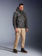 Męski model w kurtce Alpinestars Mospher Waterproof Jacket w kolorze czarnym, wodoodporna parka inspirowana stylem utility z wieloma kieszeniami i kapturem, zestawiona z beżowymi spodniami cargo i czarnymi wysokimi sneakersami, miejska odzież motocyklowa