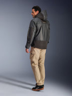 Alpinestars Mospher Waterproof Jacket w kolorze czarnym, mężczyzna widoczny z tyłu i z boku, beżowe spodnie cargo i czarne sneakersy, fason parki z kapturem, tkanina ripstop, logo Alpinestars na rękawie, nowoczesny miejski styl motocyklowy
