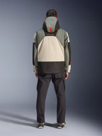 Alpinestars Mospher Waterproof Jacket, widok z tyłu motocyklisty, parka inspirowana stylem taktycznym w kolorze Fur Gray Black Ice, szare, czarne i kremowe bloki kolorów, kaptur z pomarańczowym detalem, czarne spodnie cargo