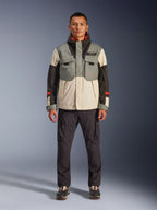 Alpinestars Mospher Waterproof Jacket w kolorze Fur Gray Black Ice, motocyklowa parka w stylu taktycznym noszona przez męskiego modela z ciemnymi spodniami cargo, konstrukcja z wieloma kieszeniami i panelami w blokach kolorystycznych szarym, kremowym i czarnym, miejska odzież motocyklowa