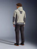 Męski model widoczny od tyłu w kurtce Alpinestars Moblast Waterproof Jacket w kolorze Iron Gray Dark Sage, miejska kurtka motocyklowa z kapturem, ciemnoszarymi panelami bocznymi i wzmocnionymi łatami na łokciach, w zestawieniu z ciemnymi spodniami motocyklowymi i czarnymi tenisówkami, nowoczesna minimalistyczna estetyka do miejskich dojazdów