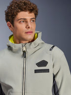Kurtka Alpinestars Moblast Waterproof, Iron Gray Dark Sage, zbliżenie na modela w kurtce, czarne logo Alpinestars i naszywki MO.ST.EQ. na klatce piersiowej, jaskrawożółta podszewka kaptura, nowoczesny techniczny design.