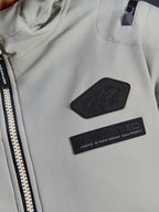 Kurtka Alpinestars Moblast Waterproof, Iron Gray, zbliżenie na naszywki na klatce piersiowej z logo Alpinestars i brandingiem MO.ST.EQ. Moto Streetwear Equipment, techniczna tkanina ripstop, solidny zamek błyskawiczny oraz detal kieszeni na ramieniu.