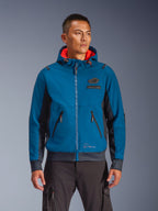 Alpinestars Moblast Waterproof Jacket prezentowana przez modela, niebieska i ciemnogranatowa miejska kurtka motocyklowa, kaptur z czerwoną podszewką, czarne zamki i naszywka na klatce piersiowej, odzież motocyklowa inspirowana stylem streetwear