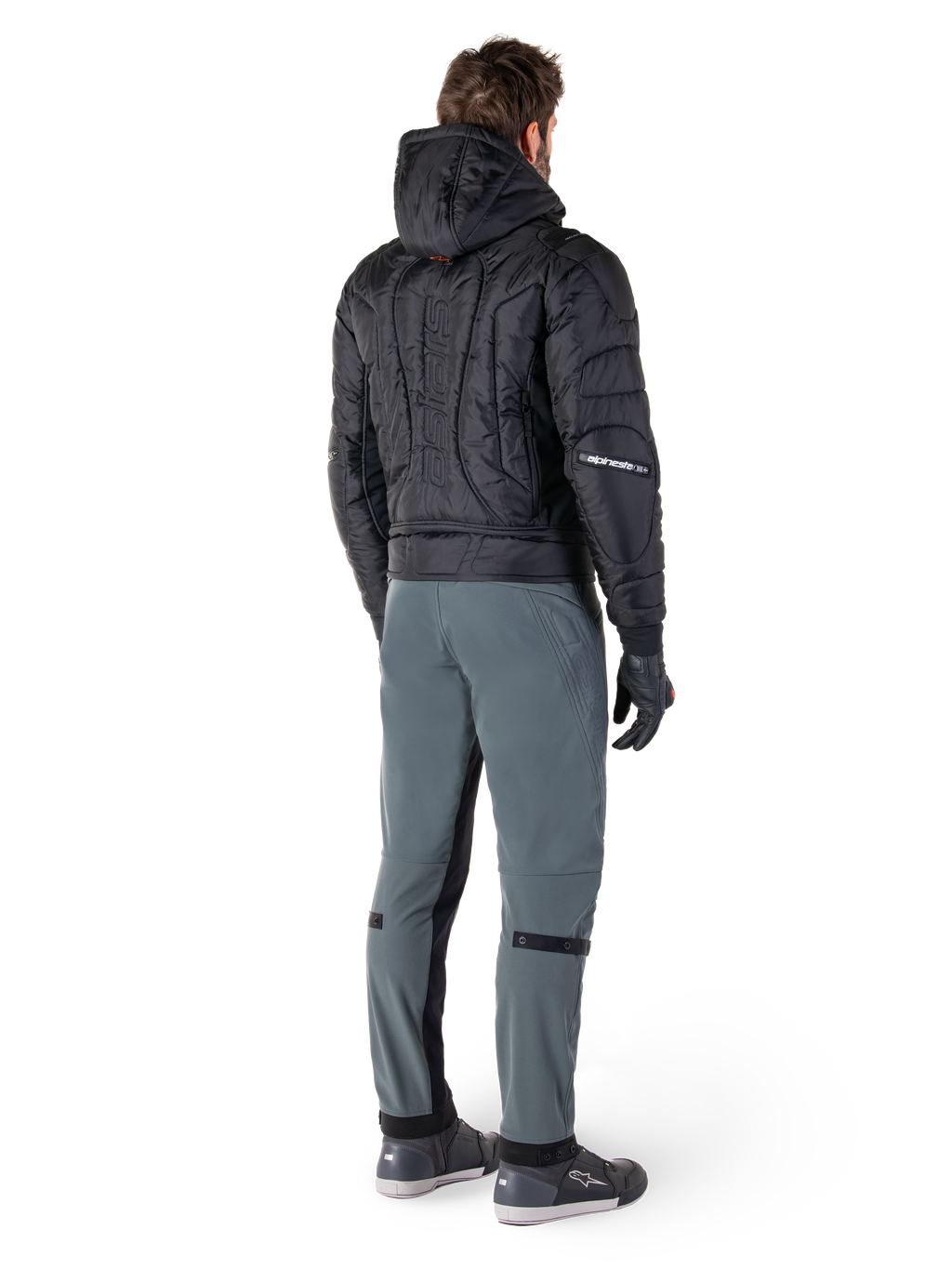 Alpinestars Mohobbs Waterproof Jacket, czarna, widok z tyłu na pikowaną kurtkę bomber z wytłoczonym pionowym napisem na plecach, zestawiona z szarymi spodniami motocyklowymi i czarnymi rękawicami, miejska odzież motocyklowa inspirowana stylem streetwear
