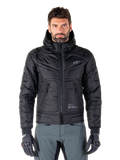 Alpinestars Mohobbs Waterproof Jacket, czarna ocieplana motocyklowa kurtka bomberka, pikowana tkanina poliestrowa z zamkiem błyskawicznym z przodu i kieszeniami na suwak, małe białe logo na piersi, noszona przez modela w szarych spodniach i rękawicach, miejski design streetwear do jazdy po mieście.