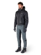 Alpinestars Mohobbs Waterproof Jacket, czarna, pikowana miejska motocyklowa kurtka bomberka z kapturem, noszona przez modela w szarych spodniach motocyklowych i czarnych rękawicach, białe logo na piersi, nowoczesna odzież ochronna inspirowana stylem streetwear