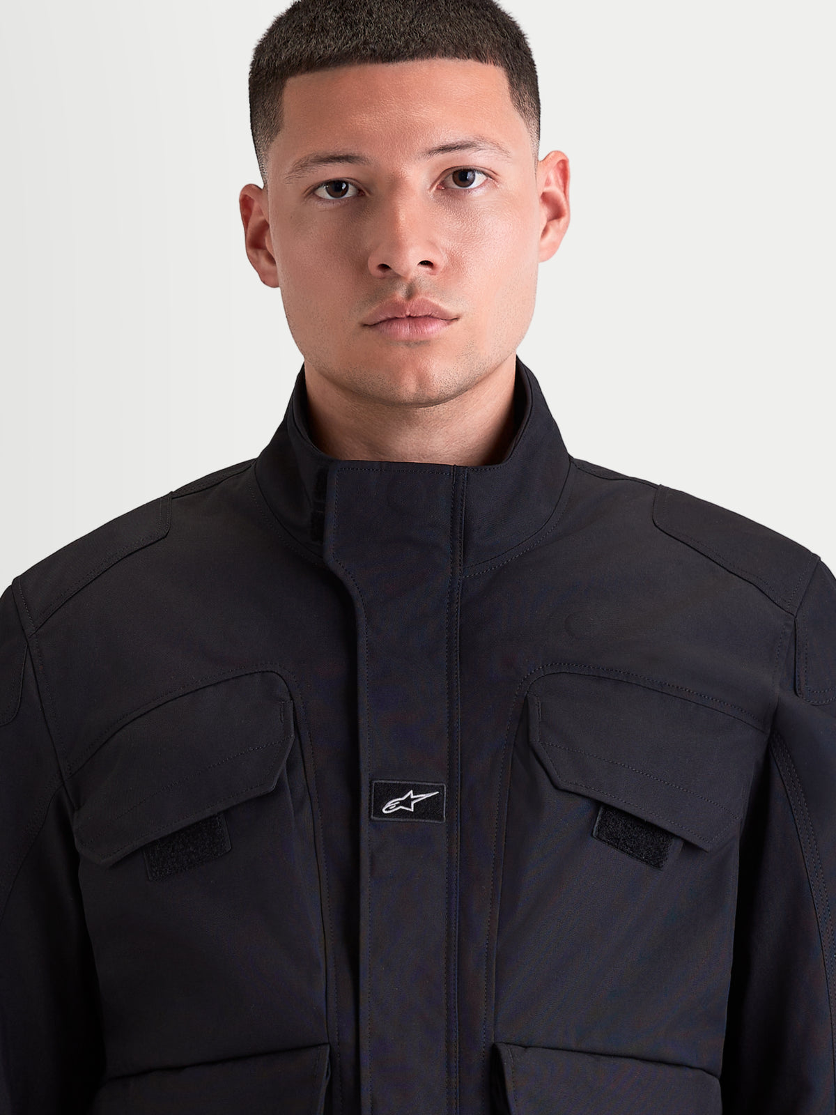 Alpinestars Altan Drystar kurtka motocyklowa męska miejska w kolorze czarnym, zbliżenie z przodu pokazujące konstrukcję z matowego materiału polyfabric, zintegrowany wysoki kołnierz oraz kieszenie cargo na piersi noszona przez modela