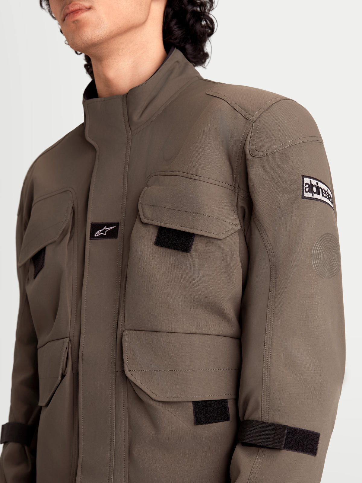 Alpinestars Altan Drystar Kurtka, męska miejska motocyklowa kurtka tekstylna w kolorze orzechowym i czarnym, zbliżenie przedstawiające kieszenie cargo w stylu kurtki polowej, matową konstrukcję z poliamidu i detale ochraniaczy ramion noszone przez modela