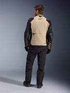 Kurtka Alpinestars Andes Pro Drystar® XF, Walnut Aluminum, widok z tyłu, motocyklowa kurtka adventure z czarnymi rękawami i czerwonymi akcentami na ramionach, noszona z czarnymi spodniami motocyklowymi i rękawicami.
