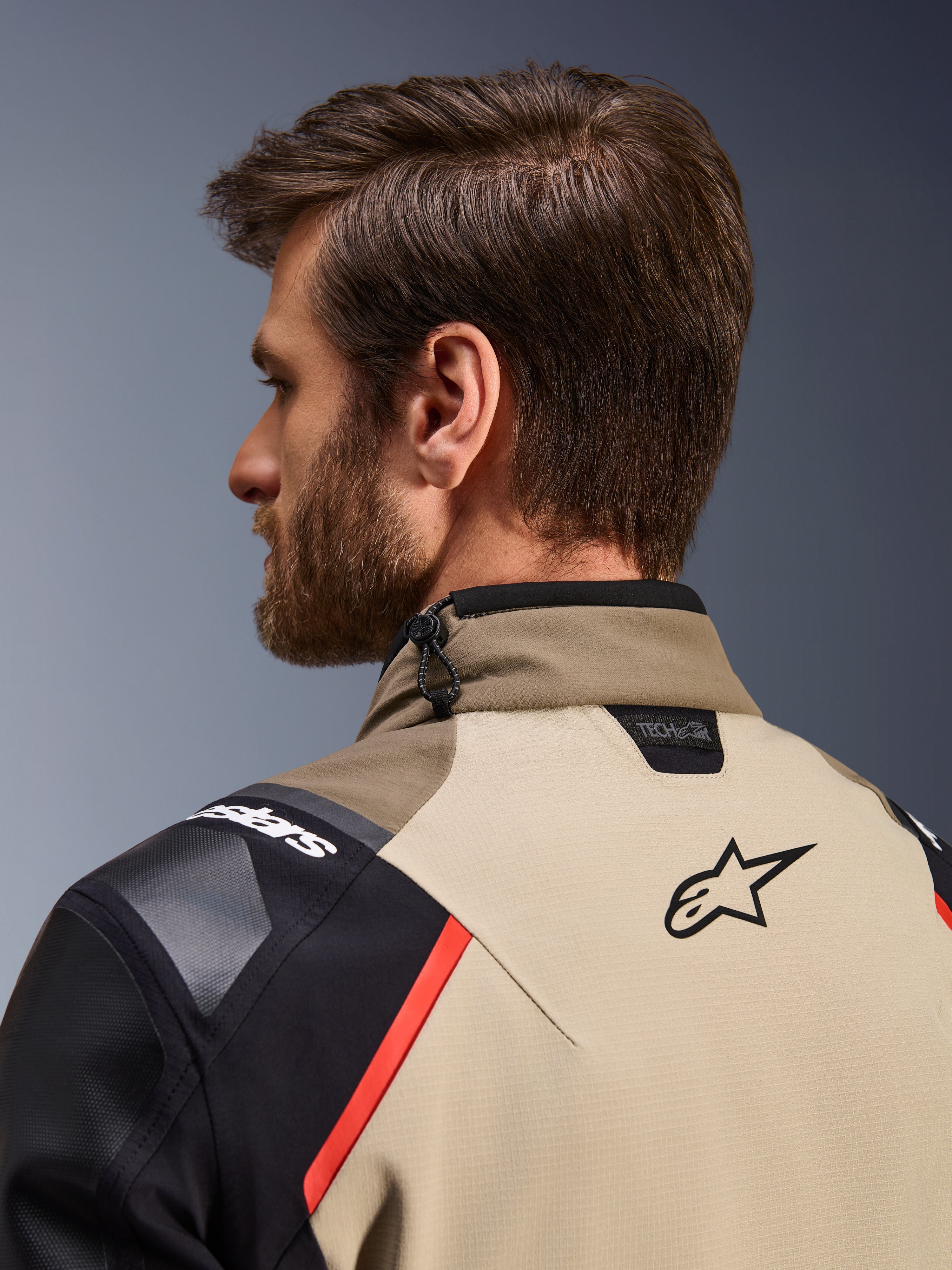 Kurtka Alpinestars Andes Pro Drystar® XF w kolorze Walnut Aluminum, widok z tyłu z bliska na kołnierz i górną część ramion, zawiera logo Alpinestars, oznaczenie kompatybilności Tech-Air, czerwone akcenty oraz system regulacji kołnierza sznurkiem amortyzującym.
