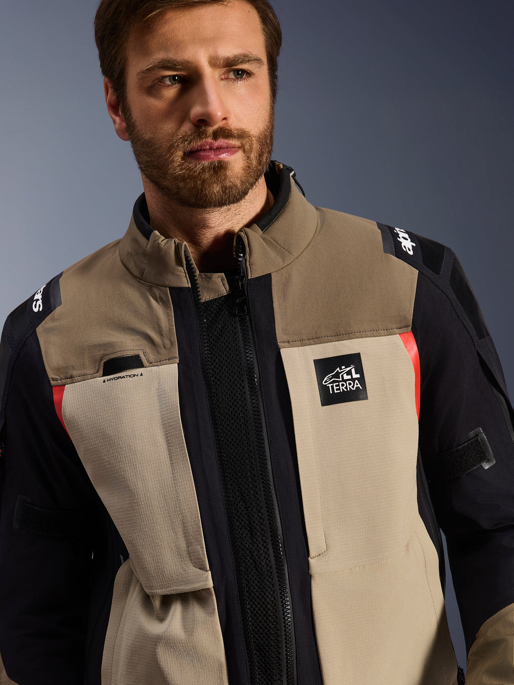 Kurtka Alpinestars Andes Pro Drystar® XF w kolorze Walnut Aluminum, noszona przez modela, motocyklowa kurtka typu adventure o warstwowej konstrukcji tekstylnej w kolorze brązowym, jasnoszarym i czarnym z czerwonymi akcentami, logo Alpinestars „TERRA” na piersi i widoczne detale techniczne