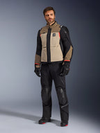Męski model ubrany w kurtkę Alpinestars Andes Pro Drystar® XF w kolorze Walnut Aluminum, zestawioną z czarnymi spodniami motocyklowymi, rękawicami i butami; wielopanelowa konstrukcja w kolorach beżowym i czarnym z czerwonymi akcentami do turystyki adventure.