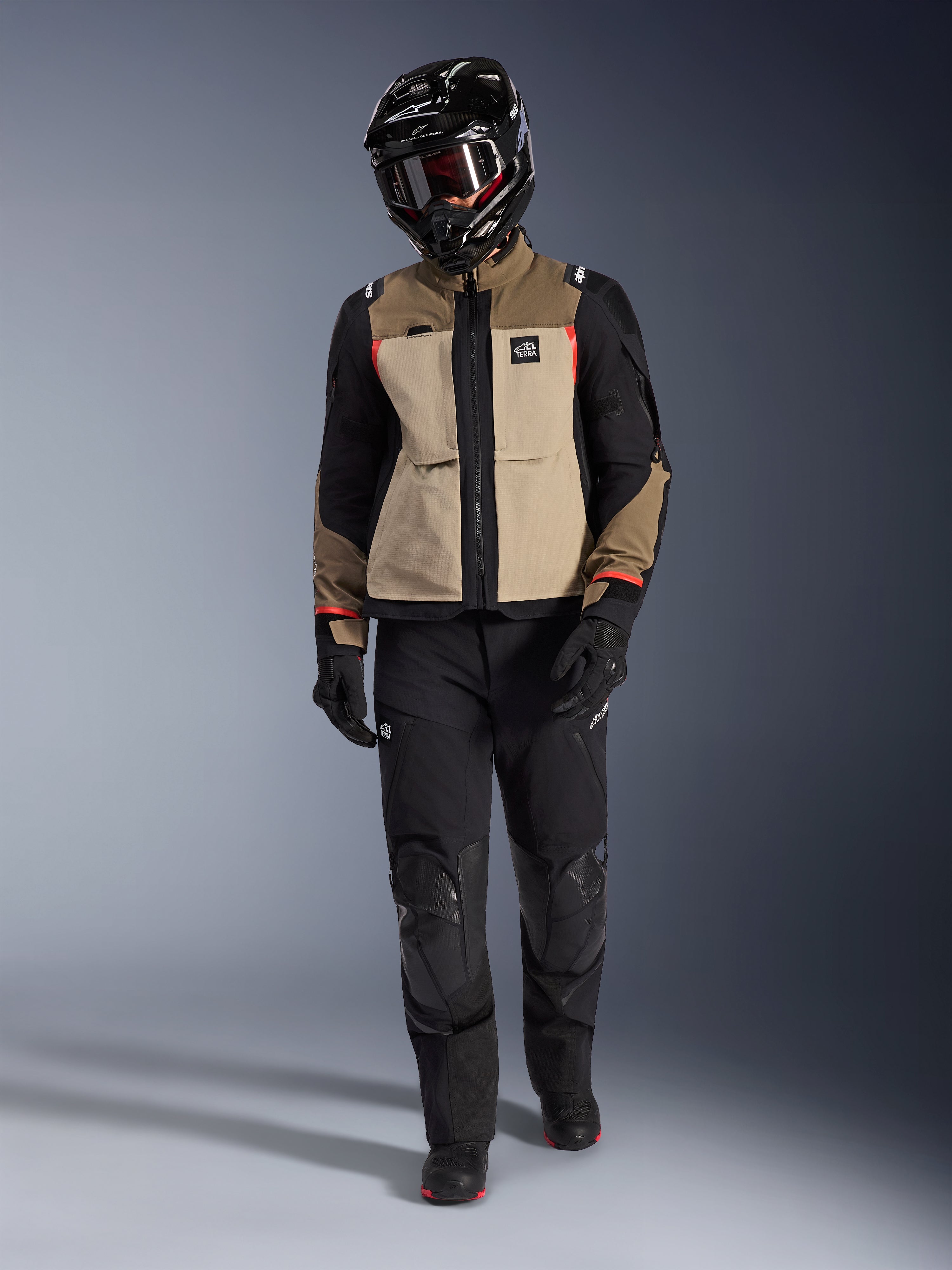 Kurtka Alpinestars Andes Pro Drystar® XF w kolorze Walnut Aluminum, zestawiona z czarnymi spodniami adventure, czarnymi rękawicami i czarnym kaskiem z goglami, z czerwonymi akcentami i brandingiem All Terra, profesjonalny zestaw adventure touring
