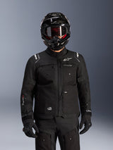 Kurtka Alpinestars Cusco Drystar®, czarna motocyklowa kurtka turystyczna adventure, noszona z czarnym kaskiem adventure i ciemnymi goglami, wyposażona w liczne kieszenie użytkowe, logo Alpinestars na klatce piersiowej i logo Drystar® na rękawie, element kompletnego stroju wyprawowego.