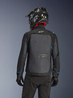 Motocyklista widziany od tyłu w kurtce Alpinestars Cusco Drystar® w kolorze czarnym i ciemnoszarym, z dużym szarym panelem wentylacyjnym na plecach i białym logo, w czarnym kasku terenowym i czarnym stroju do jazdy adventure touring.