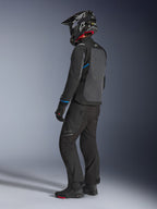 Motocyklista w kurtce Alpinestars Cusco Drystar® w kolorze czarnym i ciemnoszarym z niebieskimi akcentami, czarnych spodniach motocyklowych, kasku SM10 z włókna węglowego i czarnych rękawicach; widok z tyłu ukazujący duży panel wentylacyjny i design adventure touring.