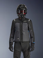 Kurtka Alpinestars Cusco Drystar®, czarna i ciemnoszara, motocyklowa kurtka adventure touring noszona z pasującymi czarnymi spodniami technicznymi i kaskiem dual-sport, dwukolorowy design z panelami ripstop i brandingiem Alpinestars