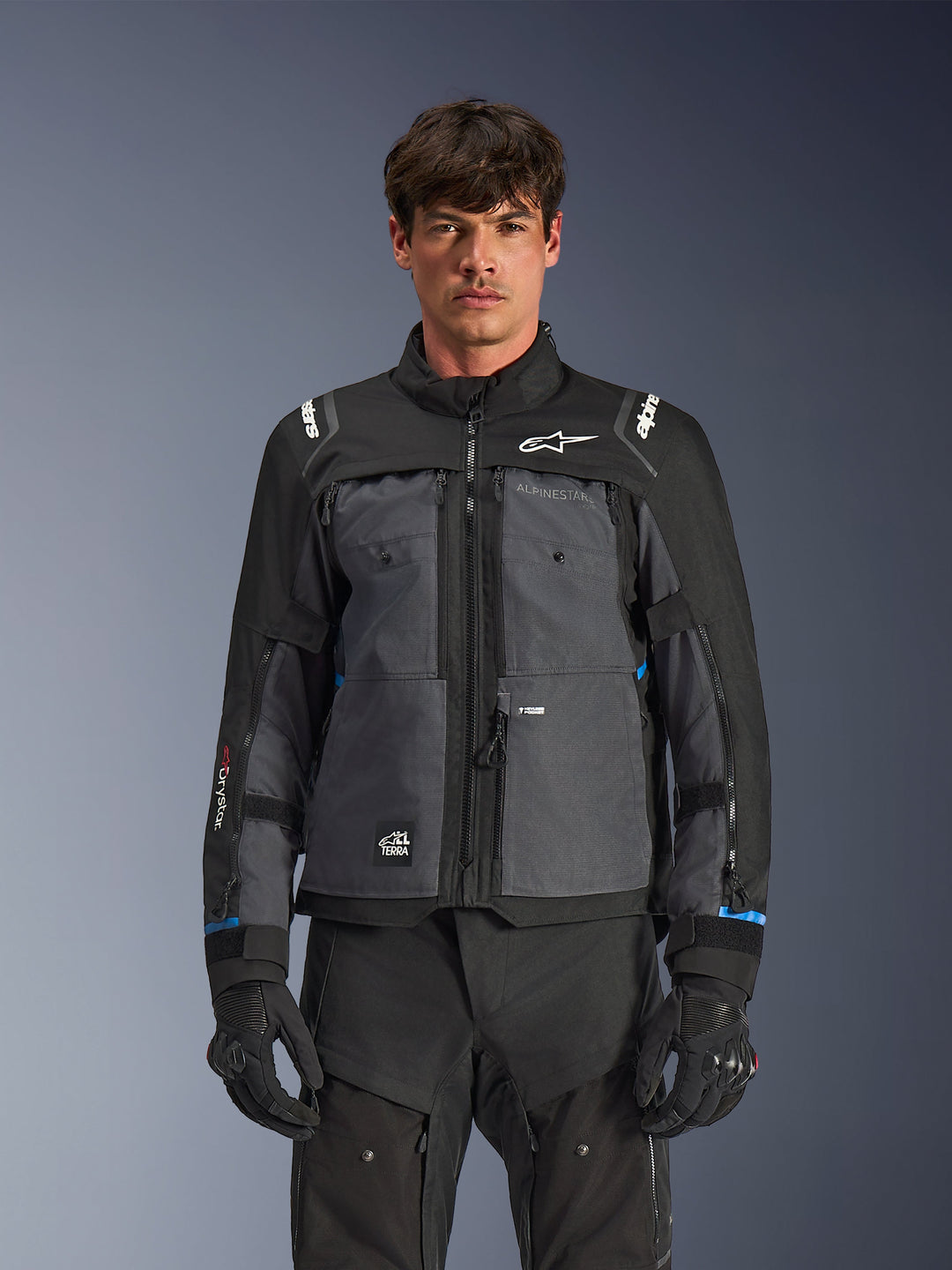 Kurtka Alpinestars Cusco Drystar®, motocyklowa kurtka turystyczna, czarna i ciemnoszara, widok z przodu na modelu, logo Alpinestars na klatce piersiowej i ramionach, branding Drystar® na rękawach, techniczna konstrukcja z wieloma kieszeniami i zamkami wentylacyjnymi, w połączeniu z czarną odzieżą motocyklową