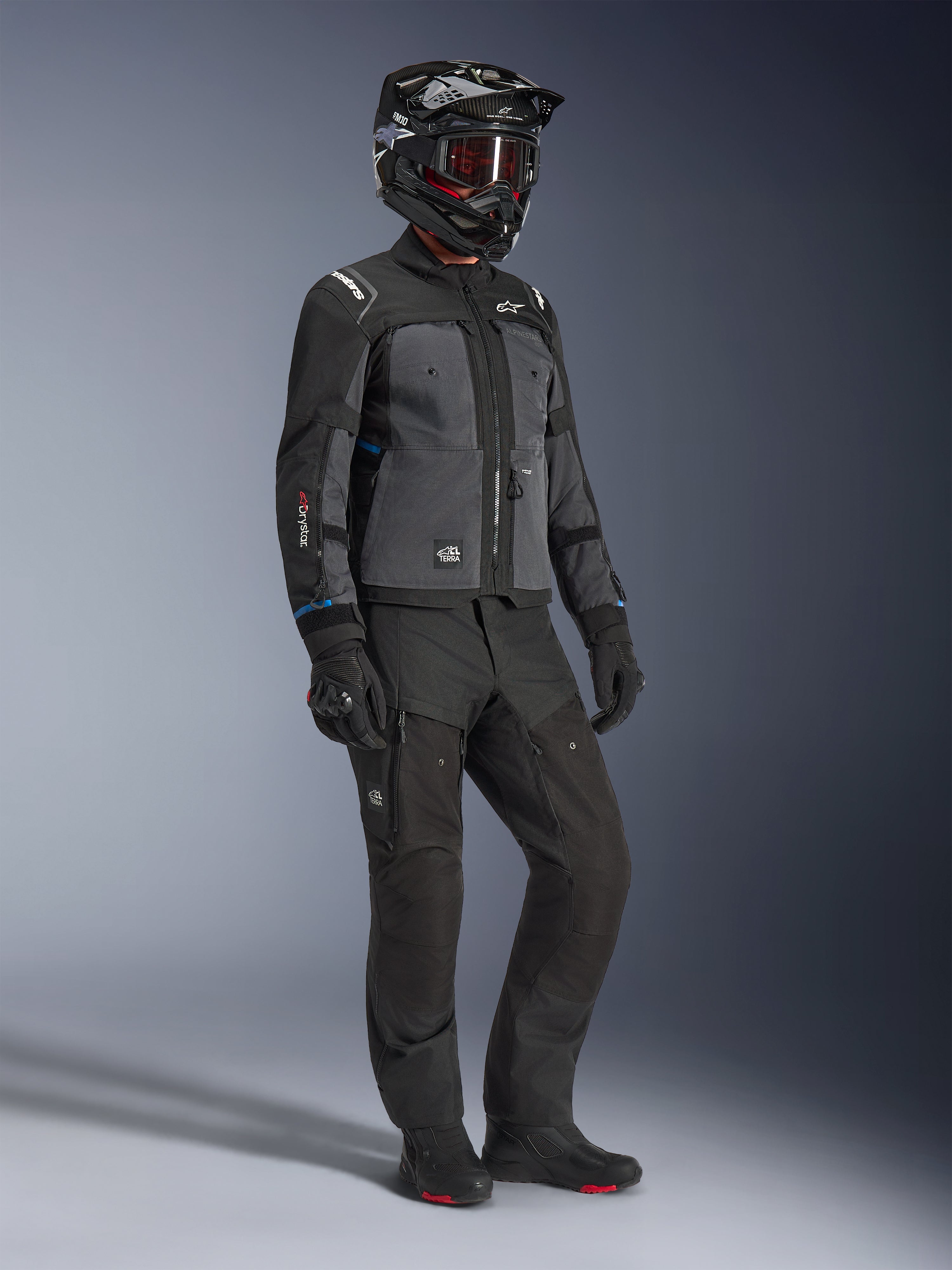 Model w kurtce Alpinestars Cusco Drystar® w kolorze czarnym i ciemnoszarym, w pełnym stroju motocyklowym z czarnym kaskiem, technicznymi spodniami, rękawicami i butami; konstrukcja ripstop i softshell do jazdy szosowej i adventure touring