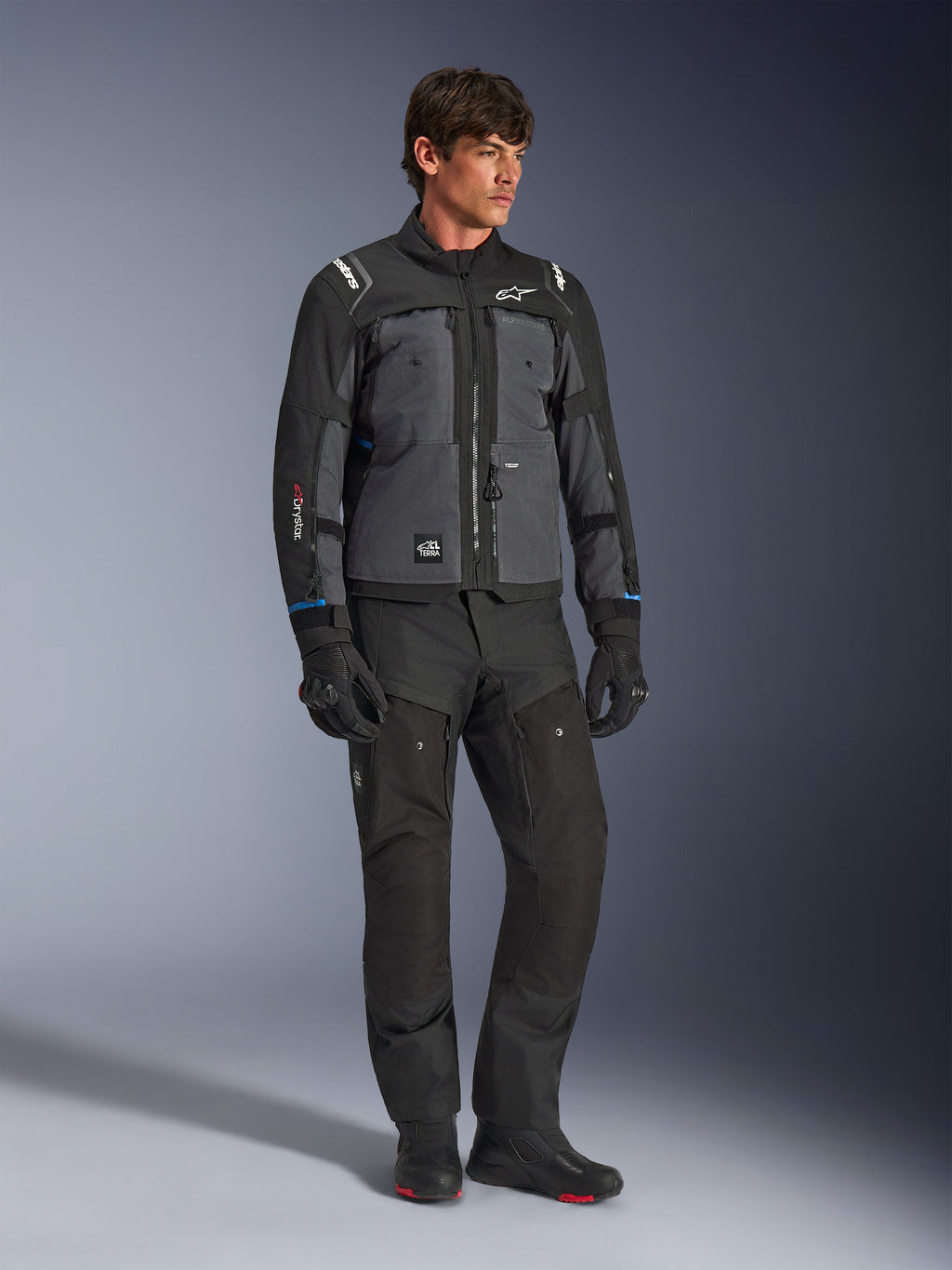 Kurtka Alpinestars Cusco Drystar® w kolorze czarnym i ciemnoszarym, techniczna motocyklowa kurtka turystyczna z wielotonowymi panelami, noszona z pasującymi czarnymi spodniami i rękawicami, zaprojektowana do jazdy szosowej i turystyki adventure.