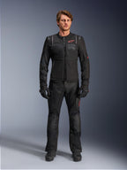 Męski model w kurtce Alpinestars ST-2 Air, czarna kurtka motocyklowa z panelami z siatki i czerwonym logo, napis „Alpinestars Exploration Equipment” na klatce piersiowej, w zestawieniu z czarnymi technicznymi spodniami i rękawicami, nowoczesny strój adventure touring