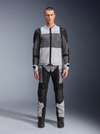 Kurtka Alpinestars ST-2 Air, motocyklowa kurtka turystyczna, kolory lodowy szary, ciemnoszary i czarny, prezentowana na modelu z dopasowanymi spodniami adventure, duże panele z siatki, niebieskie logo Alpinestars na klatce piersiowej, branding Alpinestars Exploration Equipment
