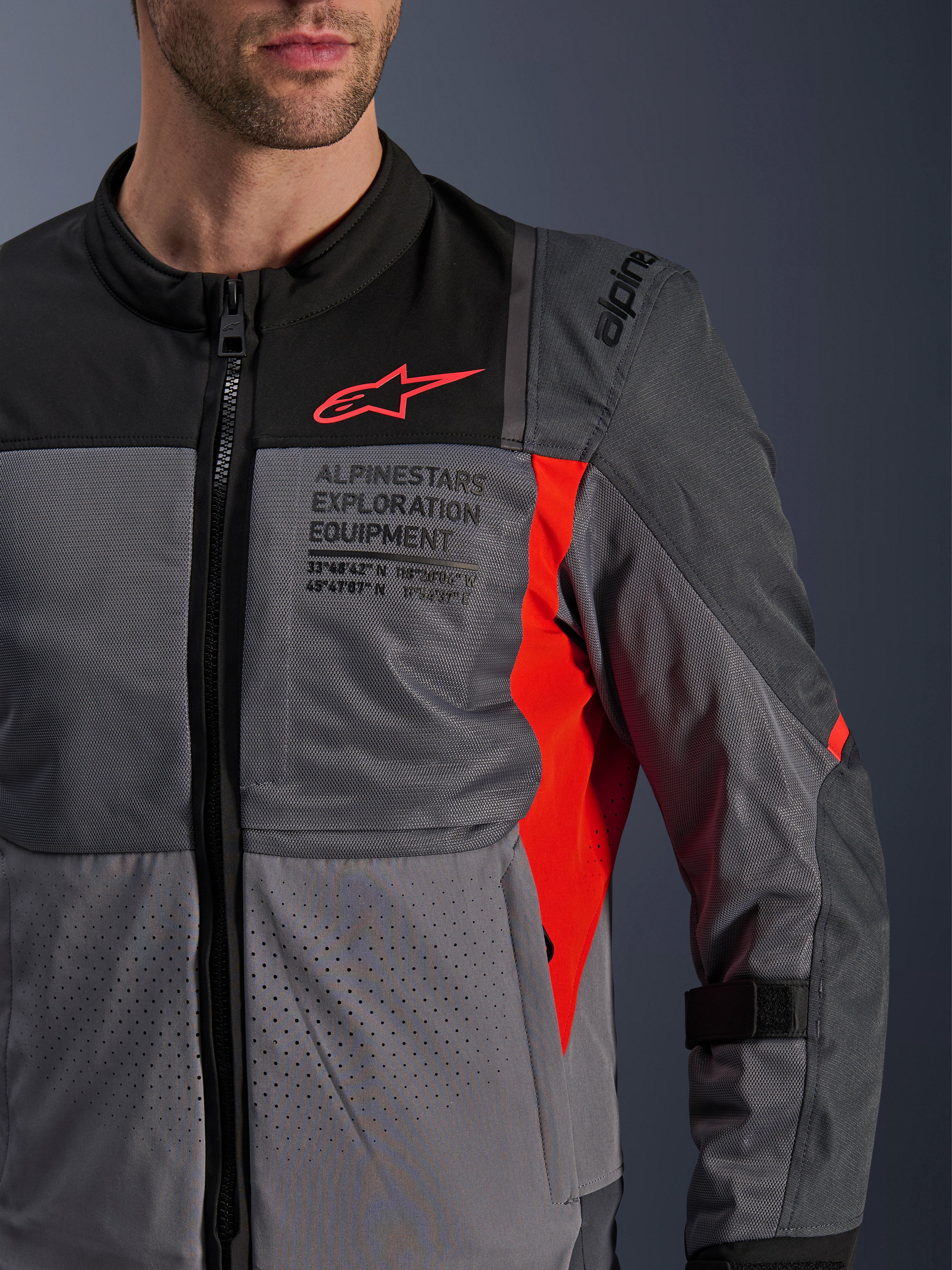 Kurtka Alpinestars ST-2 Air, tekstylna kurtka motocyklowa, ciemnoszara i grafitowa z jaskrawoczerwonymi detalami, zbliżenie na oddychające panele z siatki, laserowo perforowany materiał oraz czerwone logo gwiazdy i branding Alpinestars Exploration Equipment