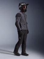 Motorcycle rider wearing Alpinestars Maxdura Drystar®XF Laminated Armored Shell jacket in Deep Gray and Black, paired with black adventure riding pants, black helmet with goggles, black gloves and boots, full-body studio shot highlighting the technical dual-sport gear.