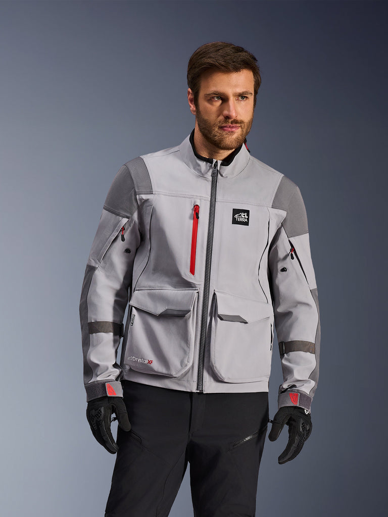 Alpinestars Maxdura Drystar®XF Laminated Armored Shell, kurtka motocyklowa adventure, średnioszary i ciemnoszary z czerwonymi akcentami, noszona przez modela w czarnych rękawicach i spodniach, wyposażona w duże kieszenie cargo i wodoodporne zamki, profesjonalna odzież motocyklowa