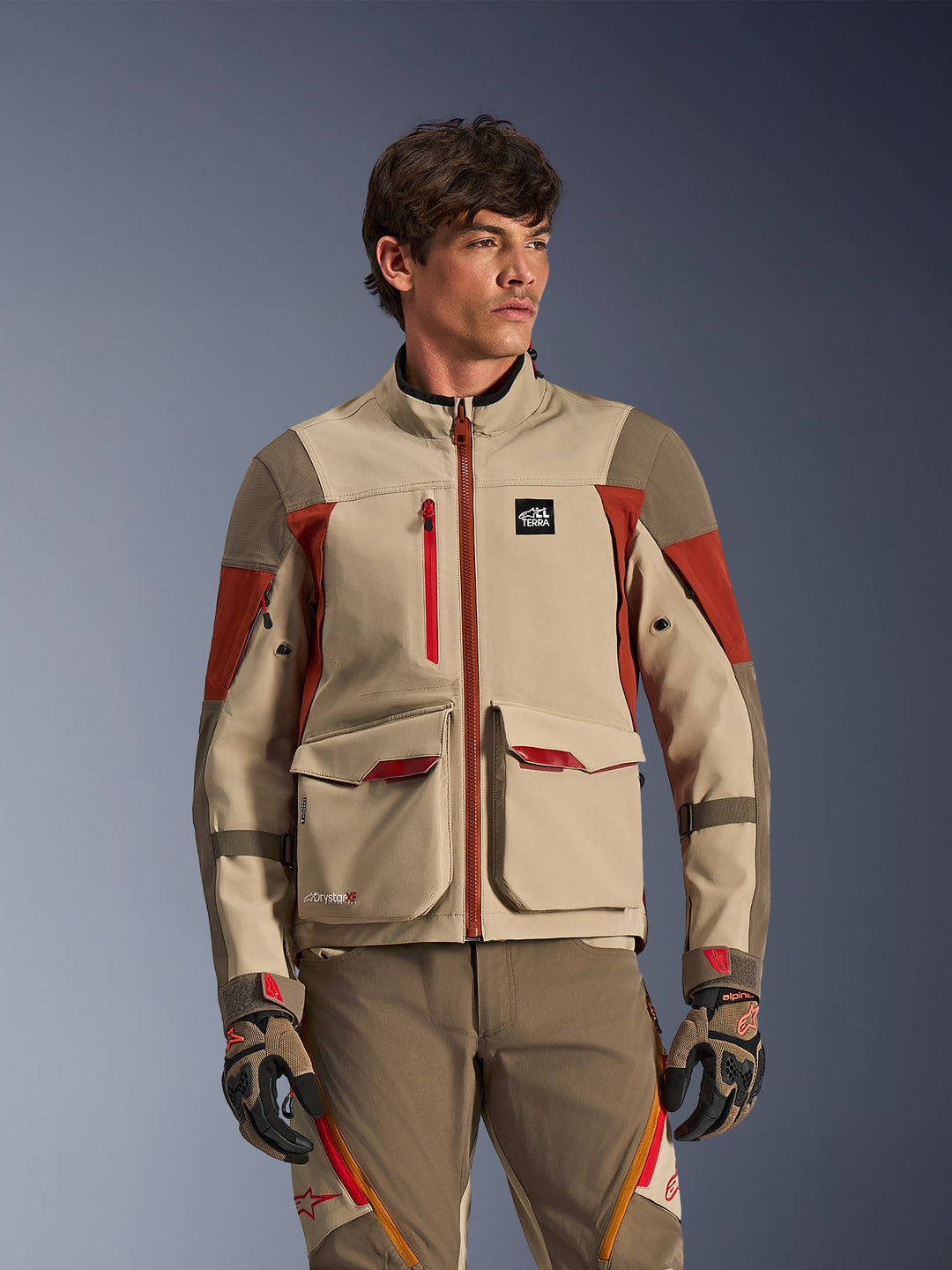 Alpinestars Maxdura Drystar®XF Laminated Armored Shell, męska kurtka motocyklowa adventure w kolorze Aluminum Walnut Rust Brown, duże przednie kieszenie cargo i techniczne czerwone akcenty, prezentowana przez modela w zestawie z pasującymi spodniami i rękawicami