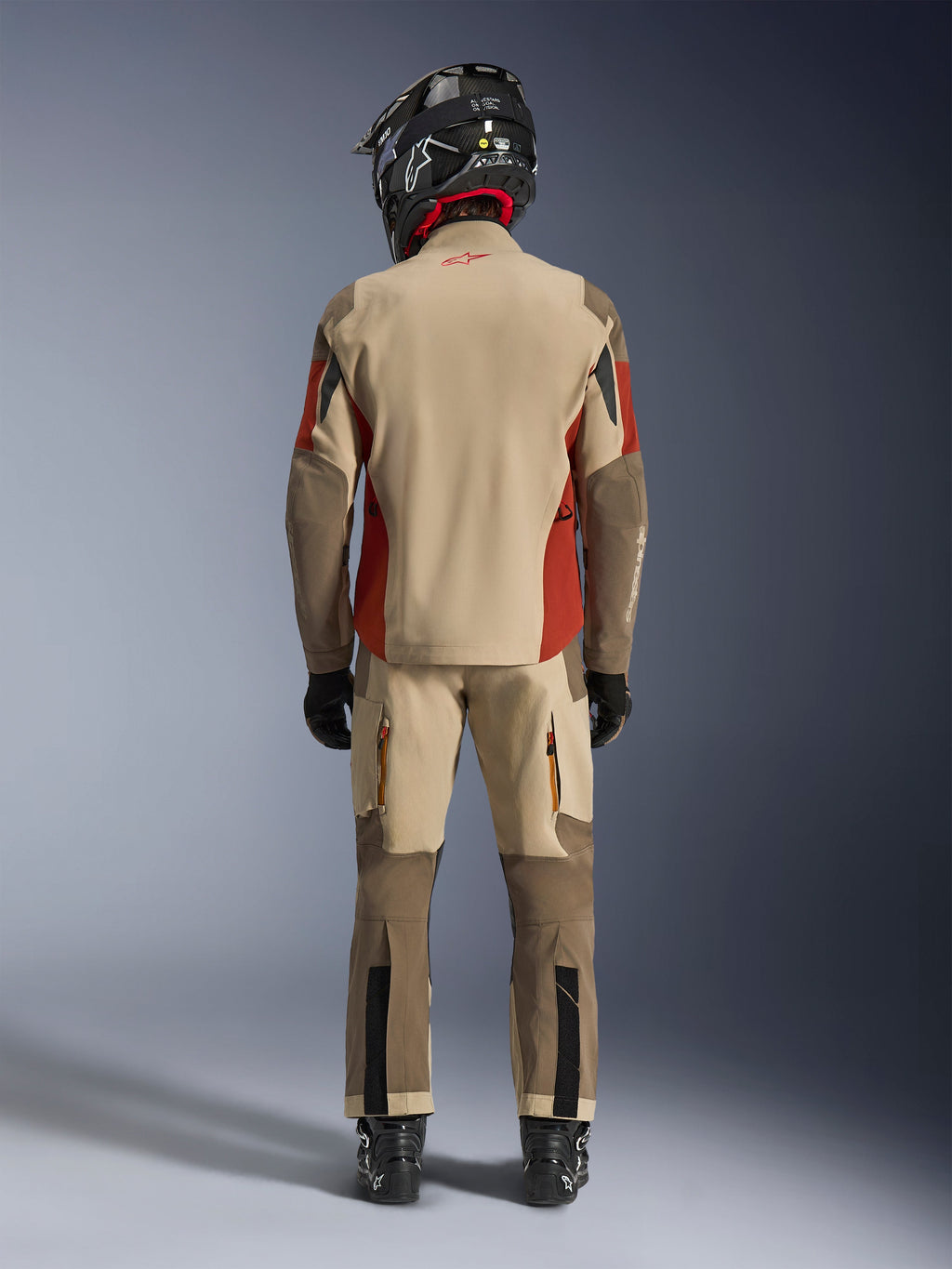 Alpinestars Maxdura Drystar®XF Laminated Armored Shell, kurtka motocyklowa adventure i pasujące spodnie, kolorystyka Aluminum Walnut i Rust Brown, widok od tyłu na motocyklistę w czarnym kasku i butach, profesjonalna odzież turystyczno-przygodowa