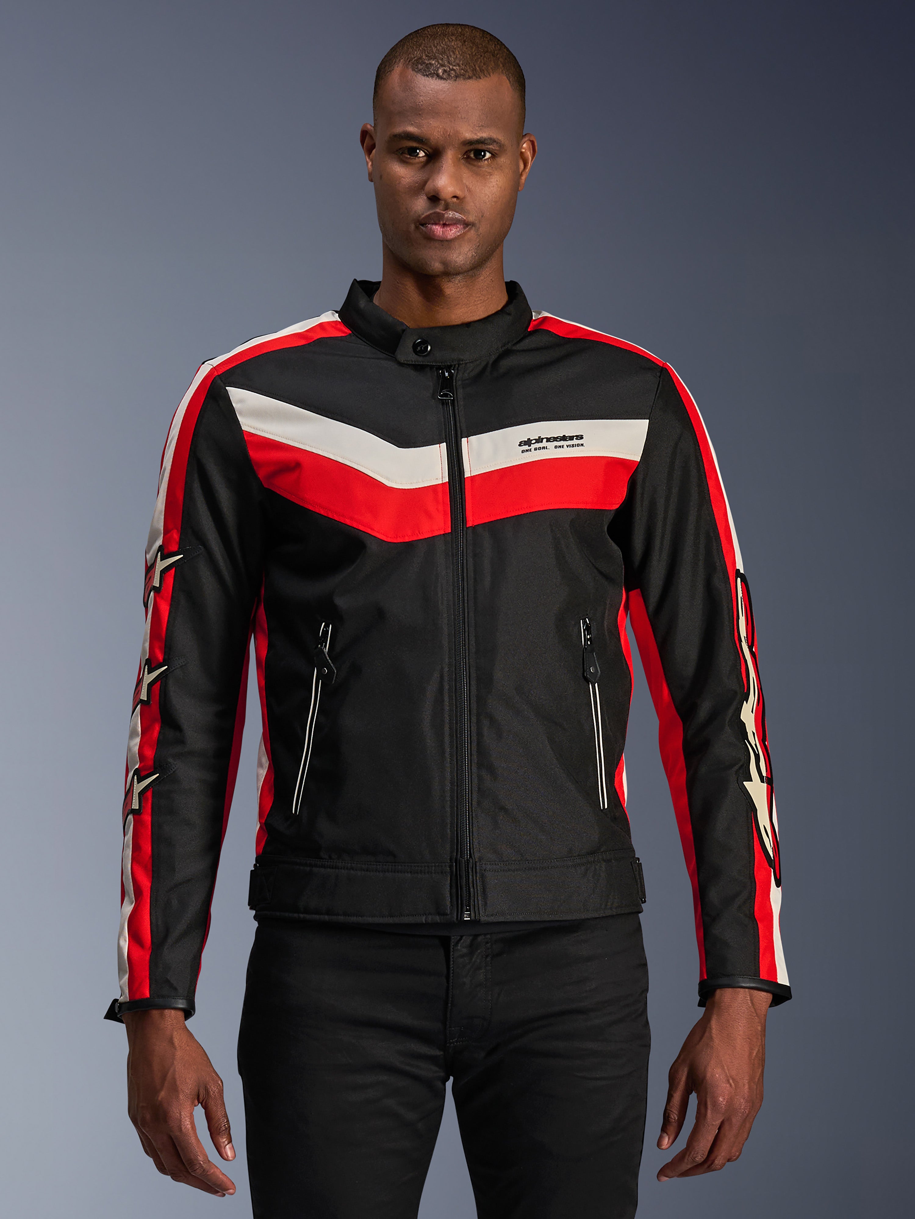 Alpinestars T-Dyno WR Jacket, tekstylna kurtka motocyklowa, czarna z jaskrawoczerwonymi i kremowymi pasami chevron, krój motocyklowy w stylu vintage, wysoki kołnierz z zapięciem na guzik, przednie kieszenie na zamek, logo z gwiazdą na rękawach, noszona przez modela
