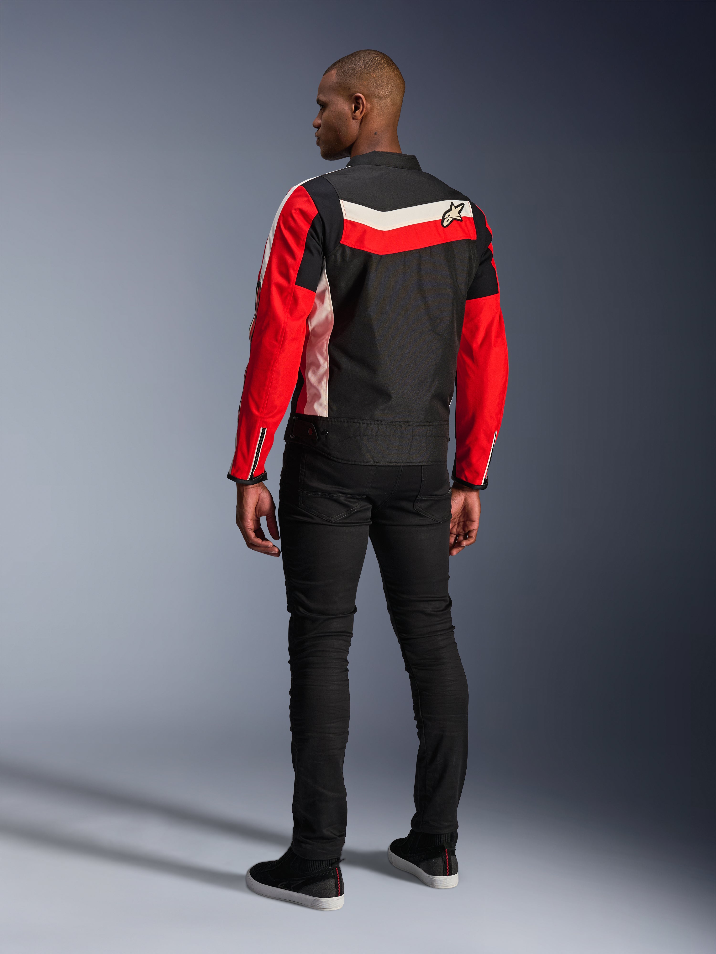 Kurtka Alpinestars T-Dyno WR, tekstylna kurtka motocyklowa, kolor czarny, jaskrawoczerwony i ecru, widok z tyłu na modelu, krój inspirowany stylem vintage z panelami kolorystycznymi i logo, nowoczesna miejska odzież motocyklowa.
