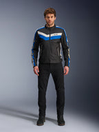 Kurtka Alpinestars T-Dyno WR, tekstylna kurtka motocyklowa, czarna, niebieska i ecru, prezentowana przez modela w czarnych spodniach i butach, z pasami w kształcie szewronu na klatce piersiowej i designem w stylu heritage biker