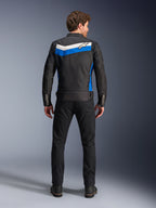 Kurtka Alpinestars T-Dyno WR, tekstylna kurtka motocyklowa, kolorystyka Black Blue Ecru, pełny widok od tyłu na modelu, z niebiesko-kremowym pasem w kształcie szewronu i logo Alpinestars, zestawiona z czarnymi spodniami i butami, miejska odzież motocyklowa inspirowana stylem vintage