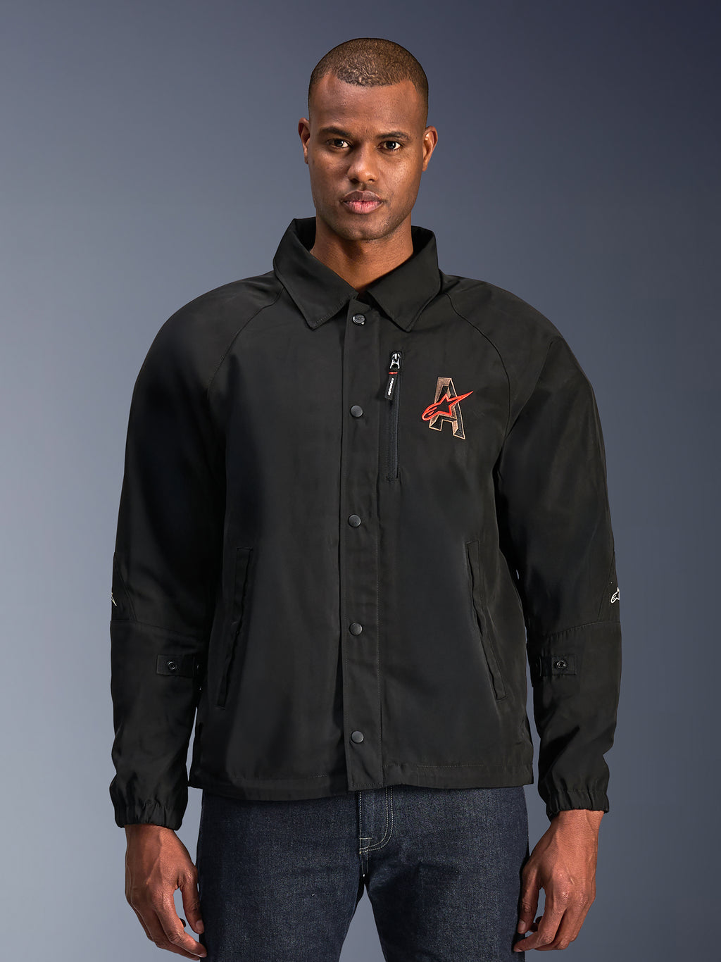 Alpinestars Revved WR Jacket, czarna kurtka motocyklowa z kołnierzykiem typu koszulowego i zapięciem na zatrzaski, czerwone haftowane logo „A” na piersi, pionowa kieszeń na zamek, elastyczne mankiety, miejski fason typu coaches jacket