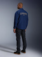 Model w kurtce Alpinestars Revved WR w kolorze granatowym, widok z tyłu, duży haft 'ALPINESTARS' z białym obramowaniem na plecach, ciemne spodnie jeansowe i czarne sneakersy, miejski styl motocyklowy