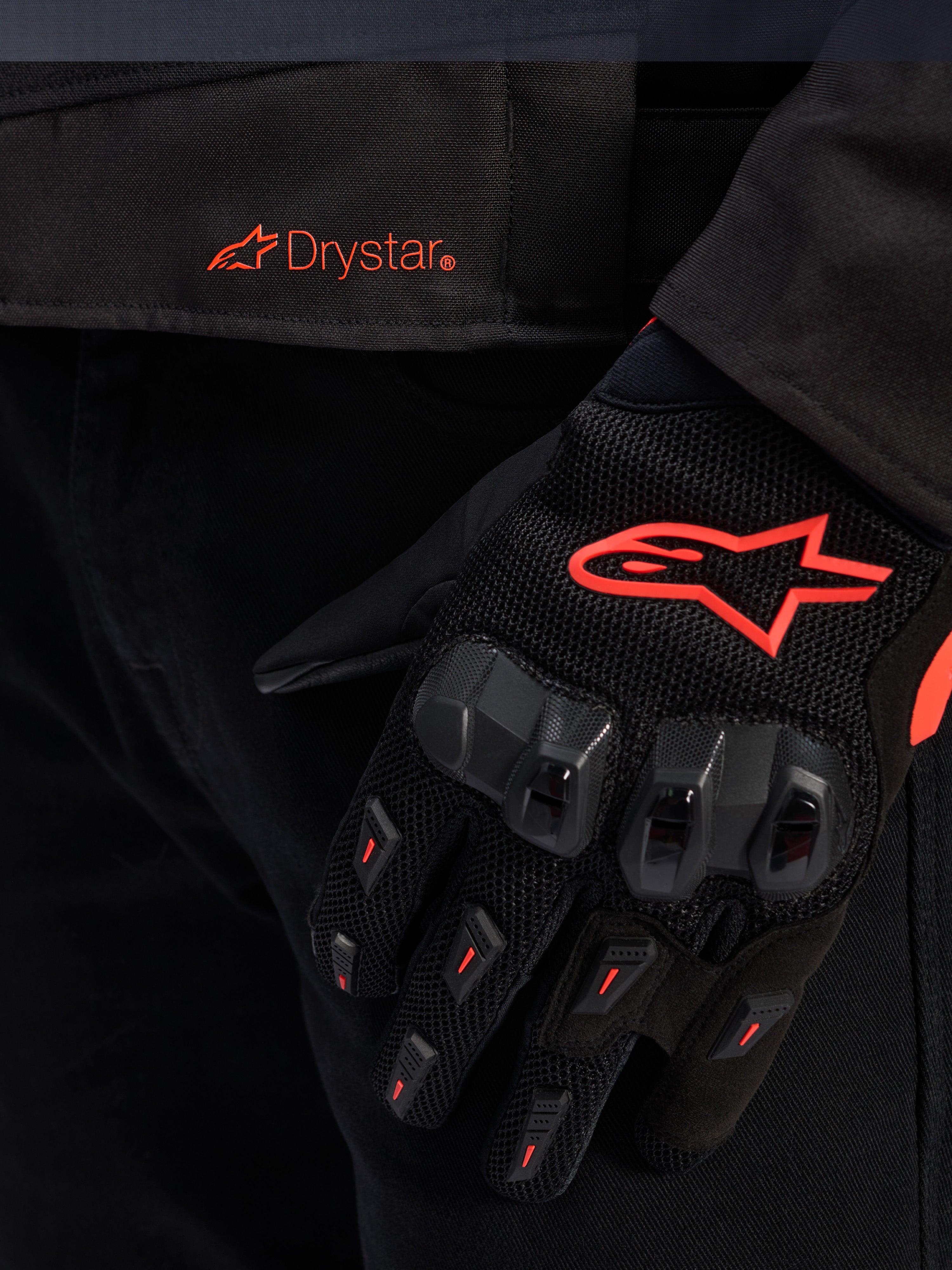 Close-up of the Alpinestars T-GP R V3 Drystar® Jacket waist featuring a red Drystar logo, shown with a black motorcycle glove with a red Alpinestars star logo, mesh fabric, and reinforced knuckle protection.