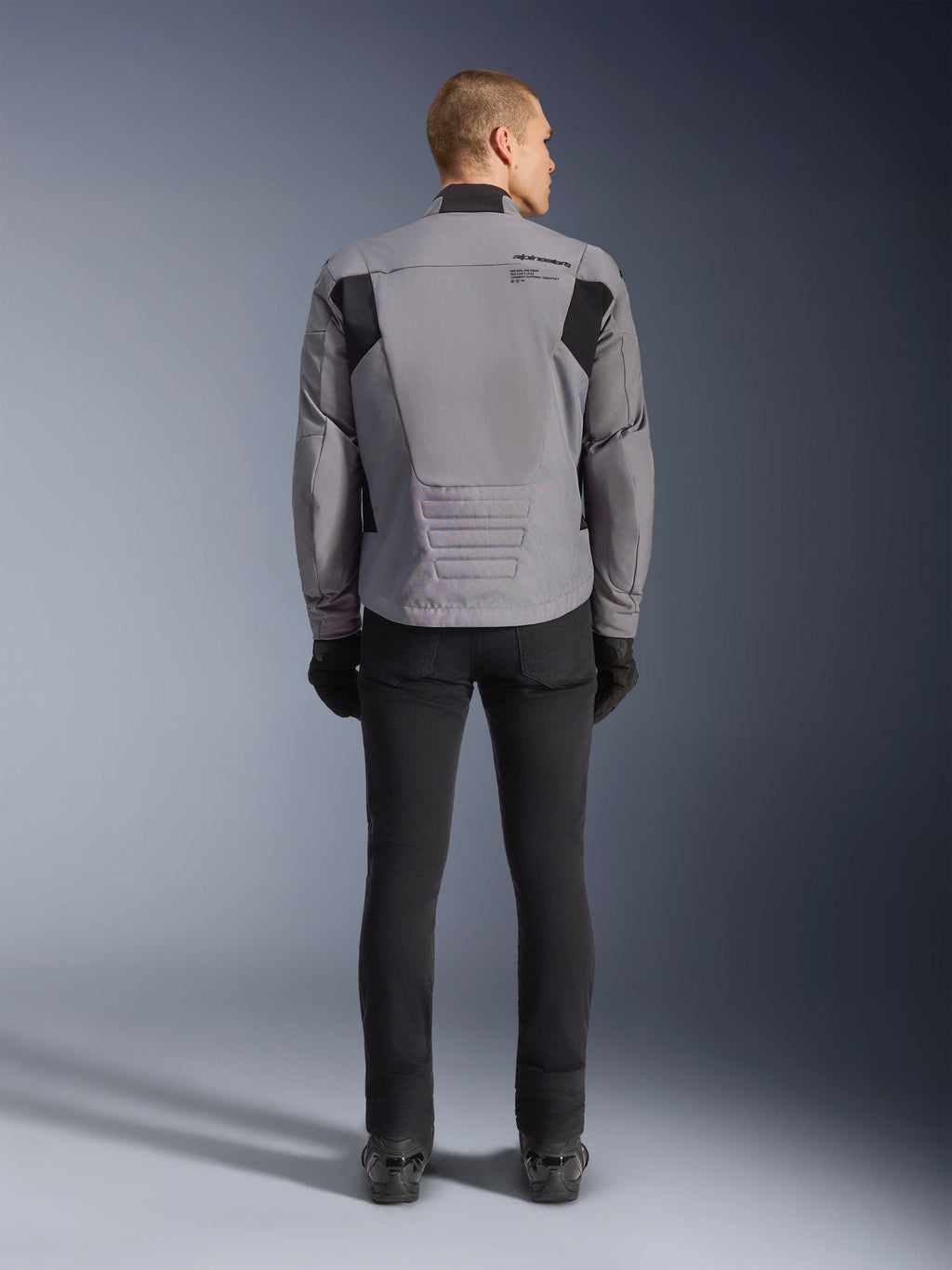 Alpinestars SMX Waterproof Jacket, widok z tyłu, kolor ciemnoszary i czarny, z czarnymi panelami tekstylnymi na ramionach i sportowym krojem, w zestawieniu z czarnymi spodniami i rękawicami dla kompletnego motocyklowego wyglądu