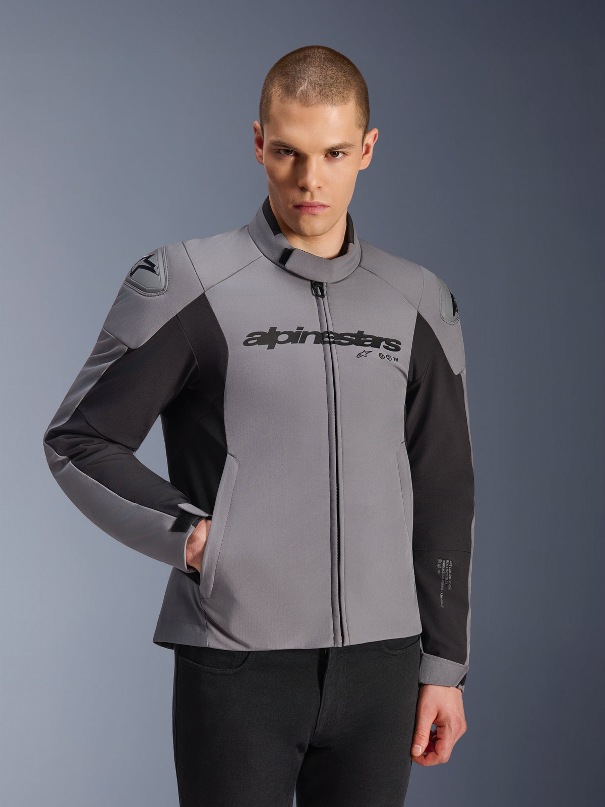 Alpinestars SMX Waterproof Jacket, ciemnoszara i czarna kurtka motocyklowa noszona przez modela, logo 'alpinestars' na piersi, ochraniacze ramion DFS Lite, sportowy design z materiałów tekstylnych i softshellowych do jazdy drogowej
