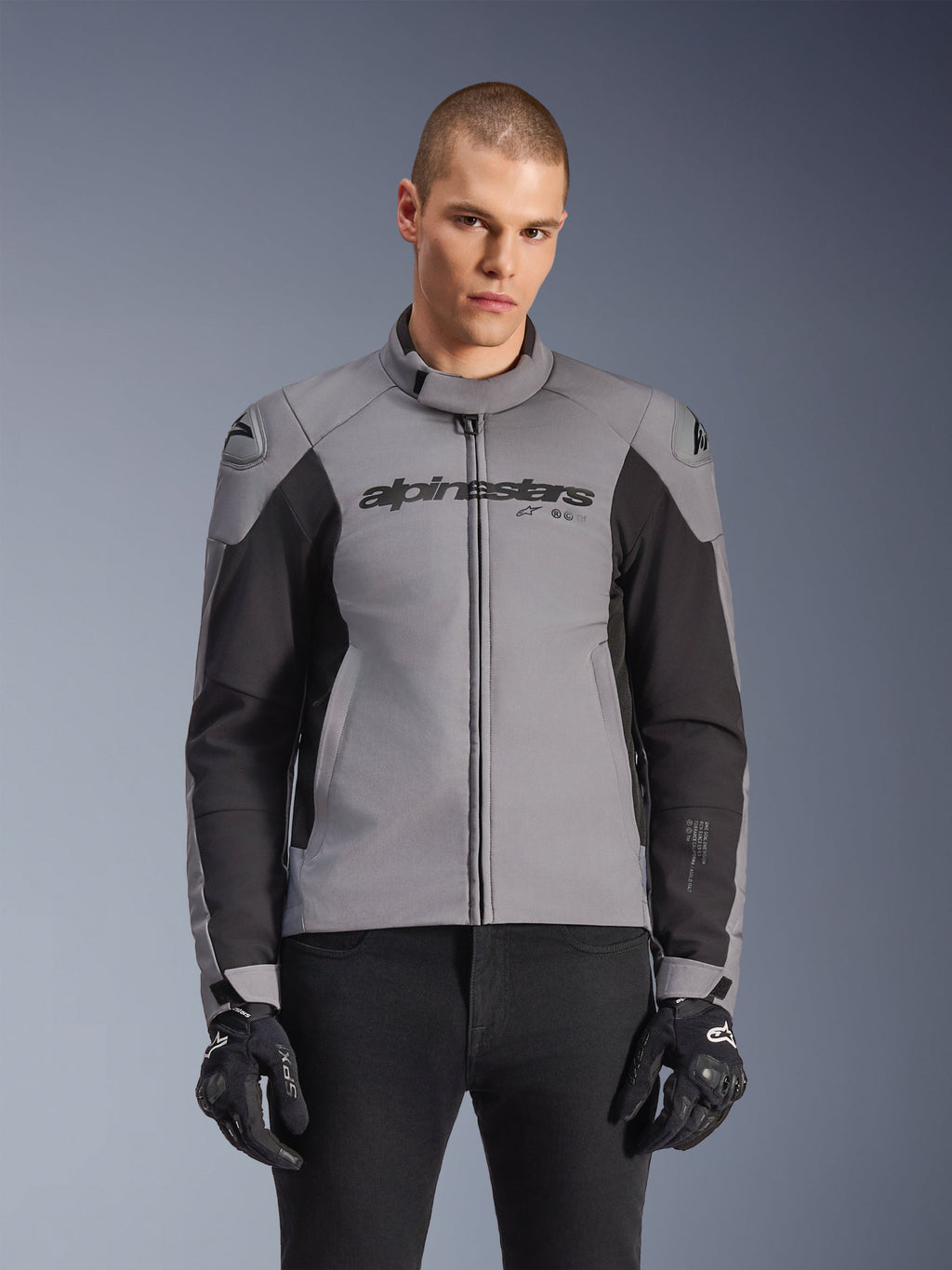 Alpinestars SMX Waterproof Jacket, sportowa drogowa kurtka motocyklowa, ciemnoszara i czarna, z wysokim kołnierzem i slajderami ramion DFS Lite, noszona z czarnymi rękawicami SMX, dopasowany sportowy krój do jazdy w każdych warunkach pogodowych
