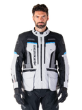 Alpinestars Bogota Pro Drystar Jacket, motocyklowa kurtka turystyczna adventure, kolor Ice Gray z czarnymi i błękitnymi akcentami, widok z przodu ukazujący panele wentylacyjne i kieszenie cargo, model w czarnych spodniach i rękawicach
